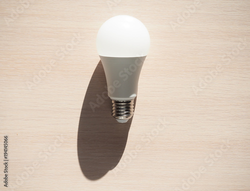 Energy saving lamp on light wooden background with hard sun shades. 