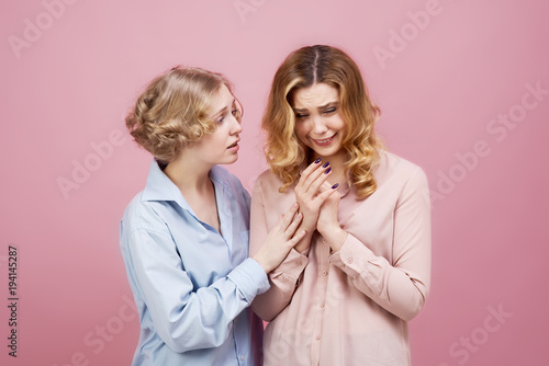 Studio portrait on pink background of two young girls. A friend comforting a crying girl and explains that all will be well. The concept of friendship, support and advice.