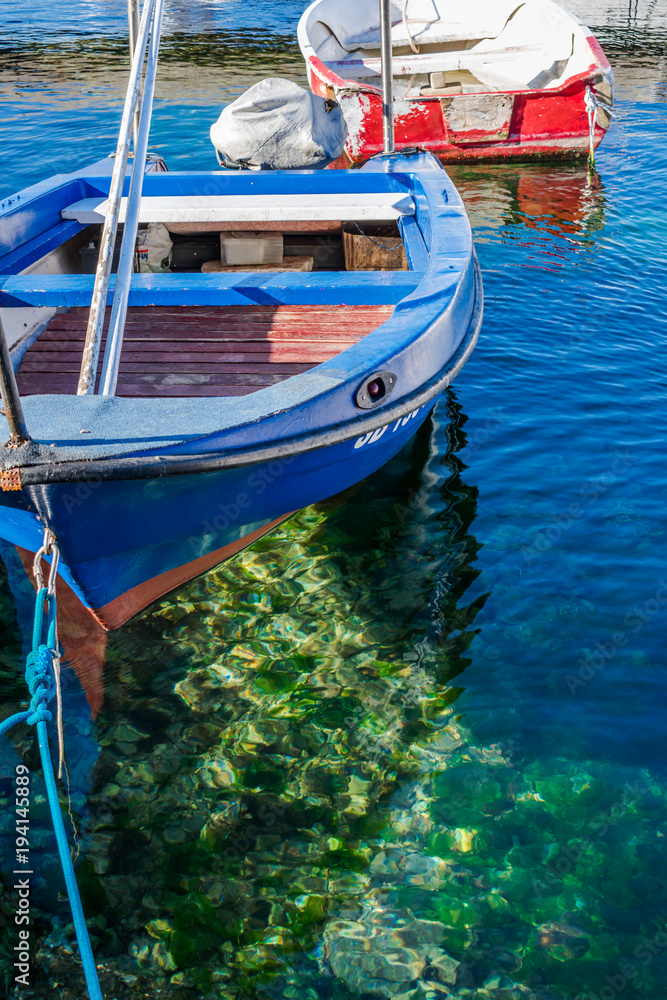 View of an old wooden traditional fishing boat floating above clear blue and green transparent sea in the village marina, Croatia
