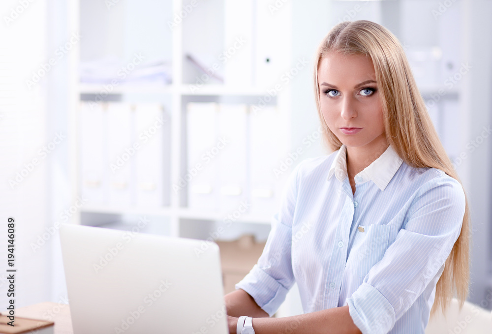 Attractive businesswoman sitting on a desk with laptop in the office Attractive businesswoman sitting on a desk with laptop in the office