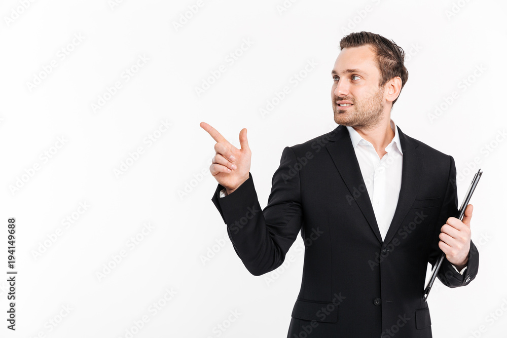 Successful businessman wearing black suit pointing finger aside and posing with folder in hand, isolated over white background copy space Successful businessman wearing black suit pointing finger aside and posing with folder in hand, isolated over white background copy space