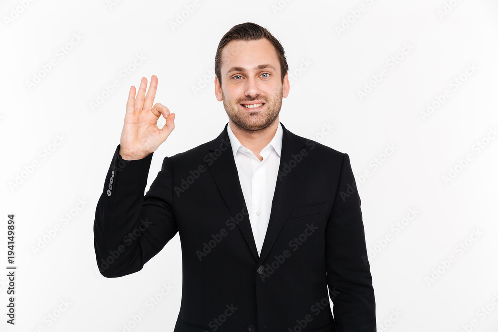 Portrait of smiling entrepreneur having stubble wearing black suit and showing OK sign meaning alright, isolated over white background Portrait of smiling entrepreneur having stubble wearing black suit and showing OK sign meaning alright, isolated over white background