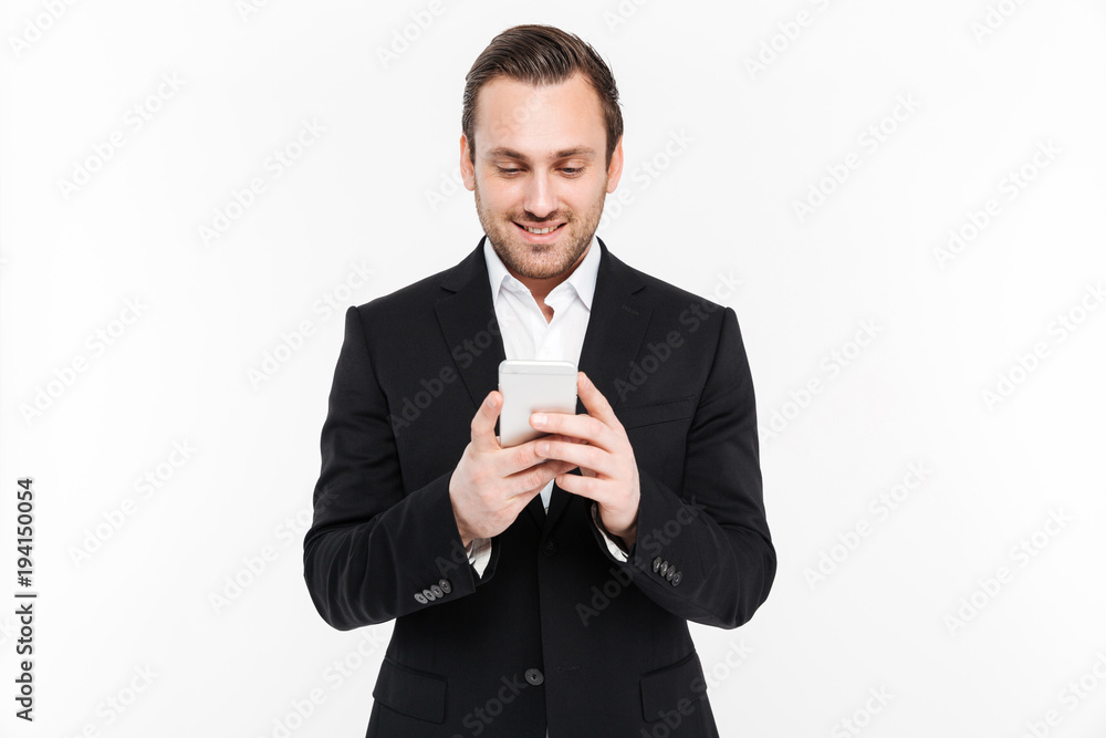 Portrait of positive man in suit posing with smile while typing sms or scrolling internet on smartphone, isolated over white background Portrait of positive man in suit posing with smile while typing sms or scrolling internet on smartphone, isolated over white background