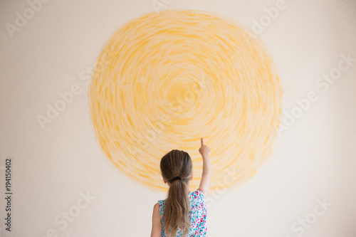 little girl points her finger at yellow sun painted on wall