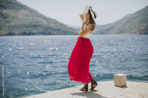 Young attractive woman with a hat poses by the sea at sunny day © BGStock72