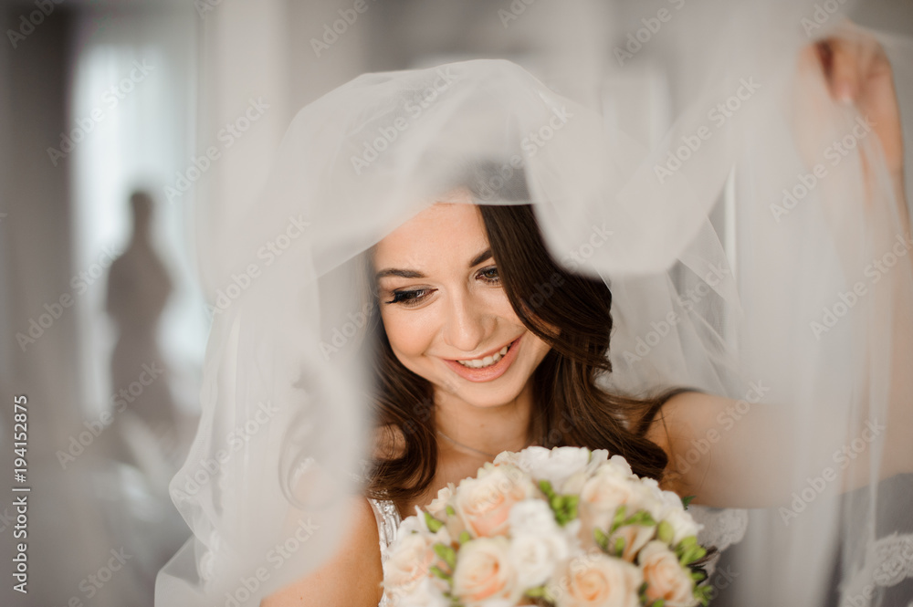 Naklejka premium Bride morning preparation. Attractive and smiling bride in a white veil with a wedding bouquet