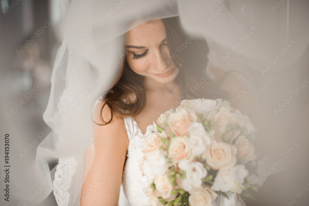 Naklejka premium Bride morning preparation. Lovely bride in a white veil with a wedding bouquet