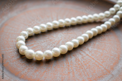 Pearl necklace on a brown clay plate. Close up of thread of white pearls on a natural background