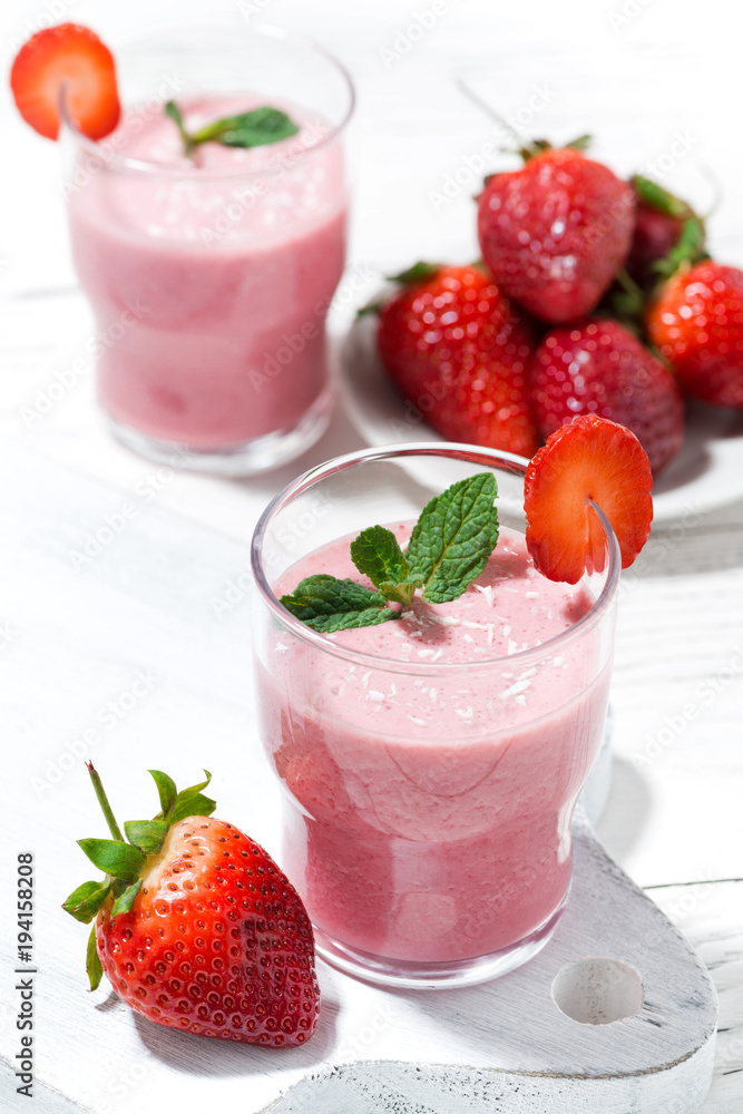glasses of refreshing strawberry milkshake on white table, vertical glasses of refreshing strawberry milkshake on white table, vertical