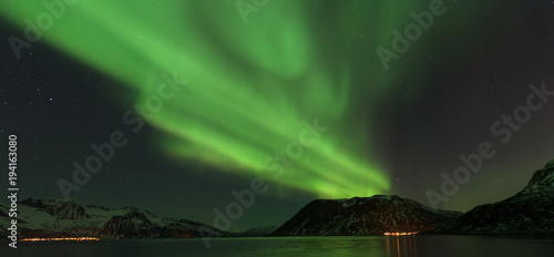 Bright green Northern Light (Aurora Borealis) lighting up the dark skies above the mountains, Tromsø, Norway