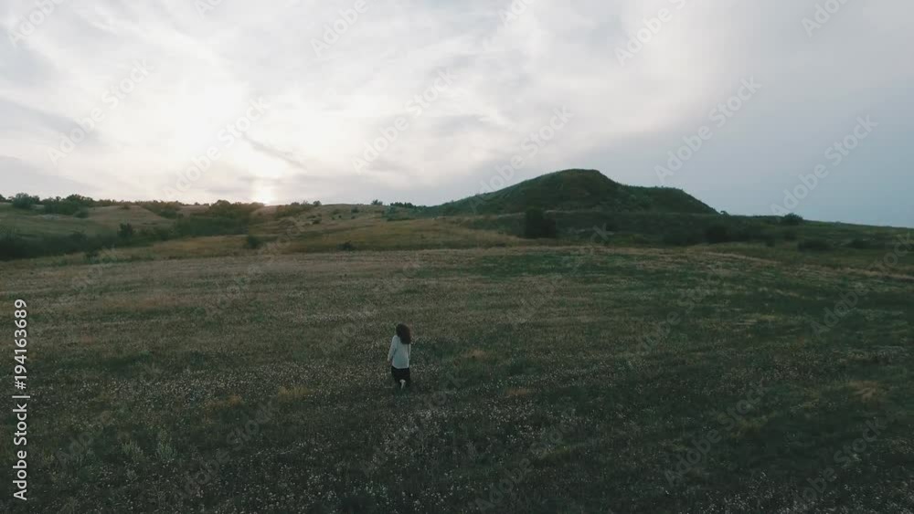 The girl in the dress is walking along the field with her arms outstretched. Obese skies overhead. Green field. The girl in the dress is walking along the field with her arms outstretched. Obese skies overhead. Green field.