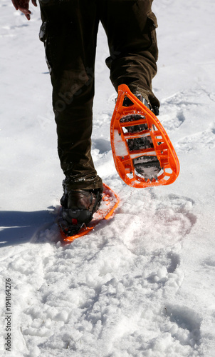 Man walks with modern orange snowshoes and corduroy pants on white fresh snow