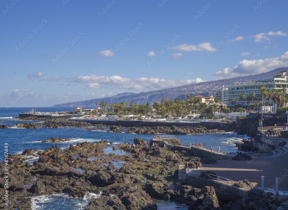 Spain, Canary islands, Tenerife, Puerto de la cruz, December 23, 2017, view on rocky sea pool with big hotel resort buildings panorama of Puerto de la cruz, tenerife with blue sky background
