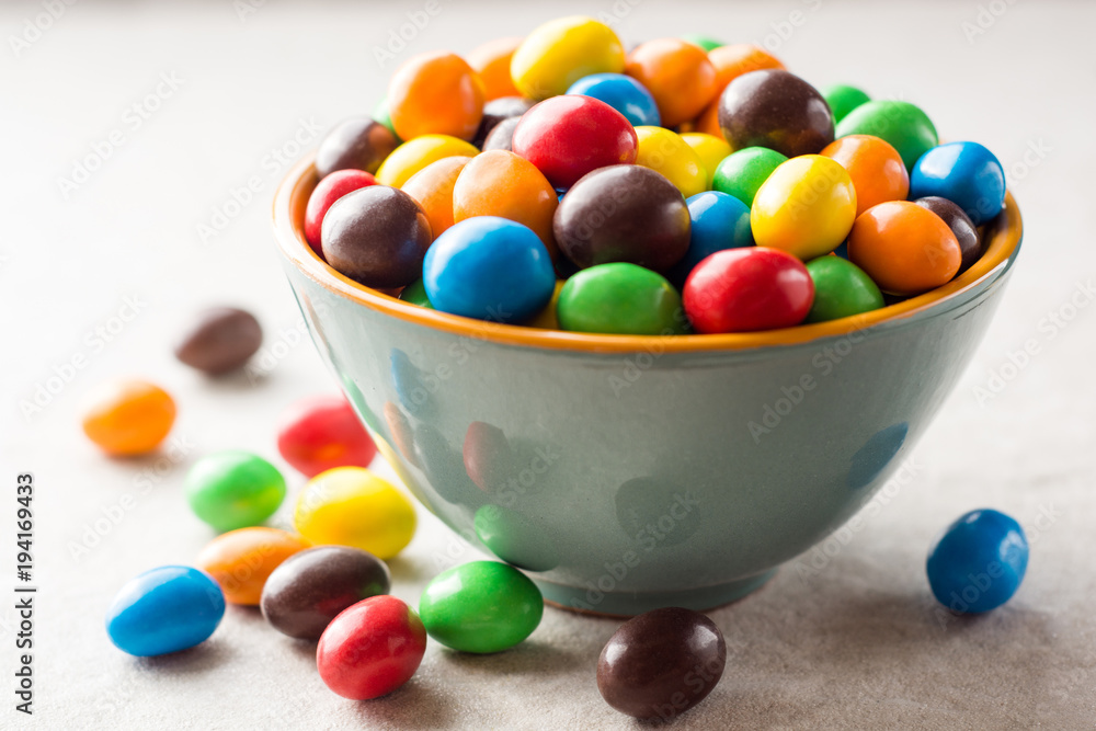 Colorful chocolate buttons in bowl on gray stone background. Colorful chocolate buttons in bowl on gray stone background.