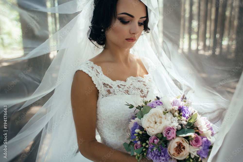 Naklejka premium Stunning young bride stands in the forest with tall trees and morning sunshine
