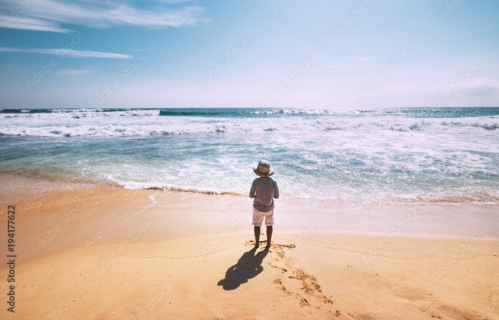 Little boy stay on ocean beach in sunny day