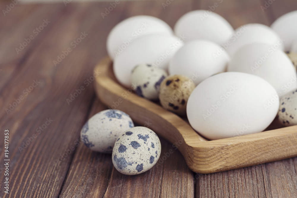 Obraz premium White eggs and quail eggs in wooden heart shaped plate on wooden brown background