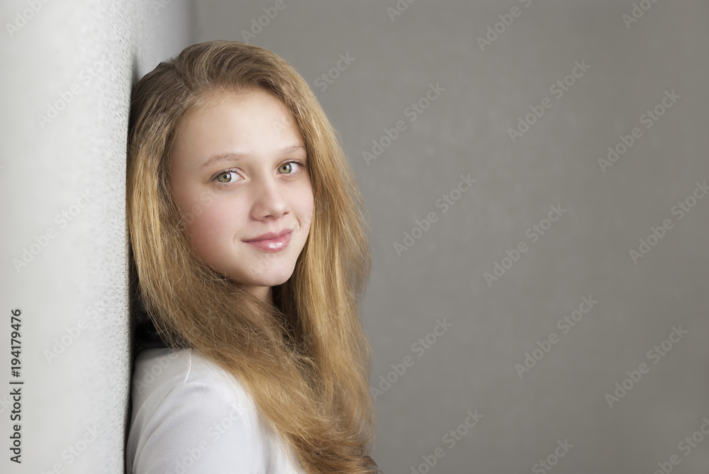 Pretty blonde girl looking in camera and smiling while standing near wall Pretty blonde girl looking in camera and smiling while standing near wall