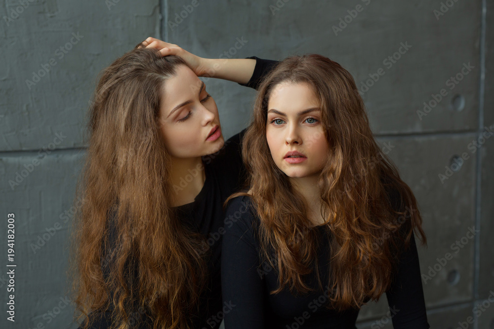 © Alexandr - portrait of two beautiful young girls of twin sisters with flowing hair against the gray wall in the interior