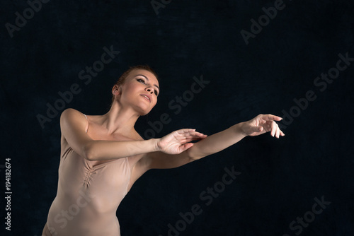 the ballerina in a beige suit from latex dances on a dark background in studio