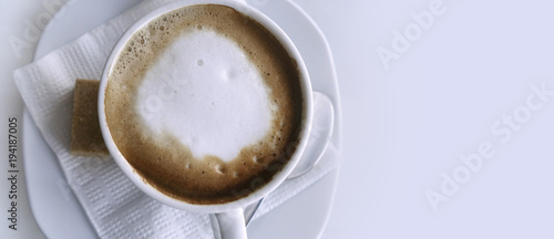 Coffee cappuccino in a white cup on a white napkin and saucer. Close-up. Place for text. View from above.
