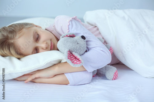 Child little girl sleeps in the bed with a toy teddy bear