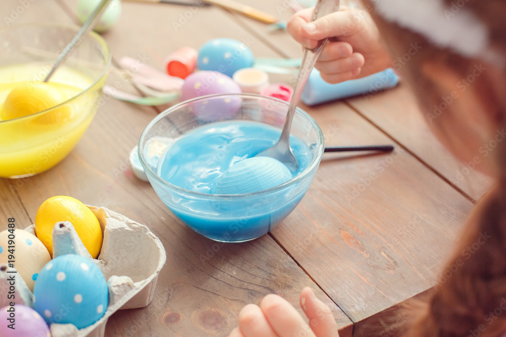 Little cute girl at home easter celebration concept back view close-up coloring eggs dipping egg into blue water Little cute girl at home easter celebration concept back view close-up coloring eggs dipping egg into blue water
