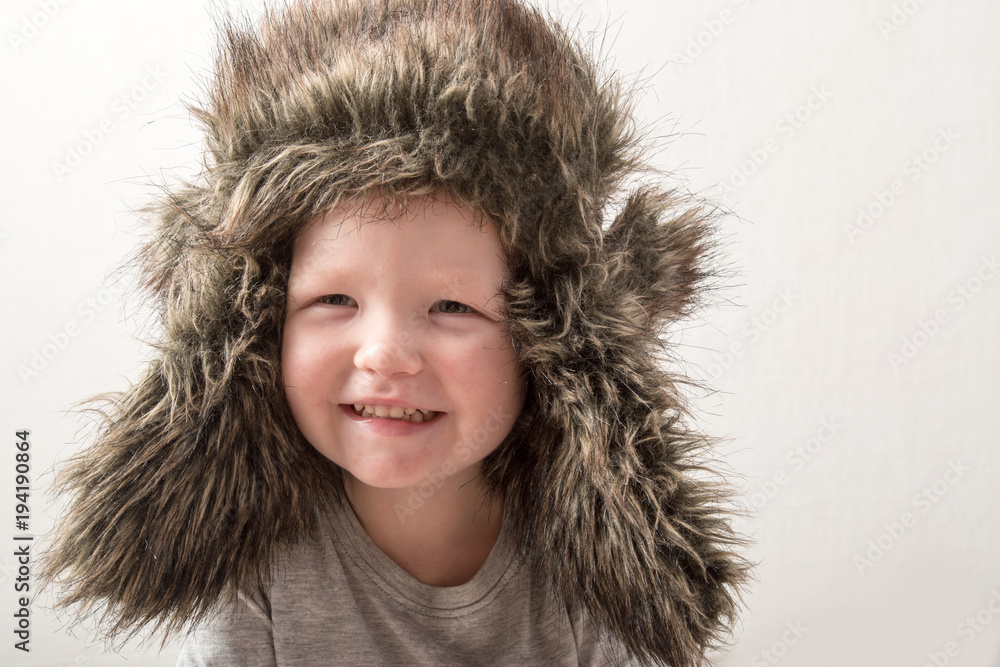 Happy child playing at home. The funny guy put on a warm fur hat and admires himself. Close-up. Portrait with emotions. Happy child playing at home. The funny guy put on a warm fur hat and admires himself. Close-up. Portrait with emotions.