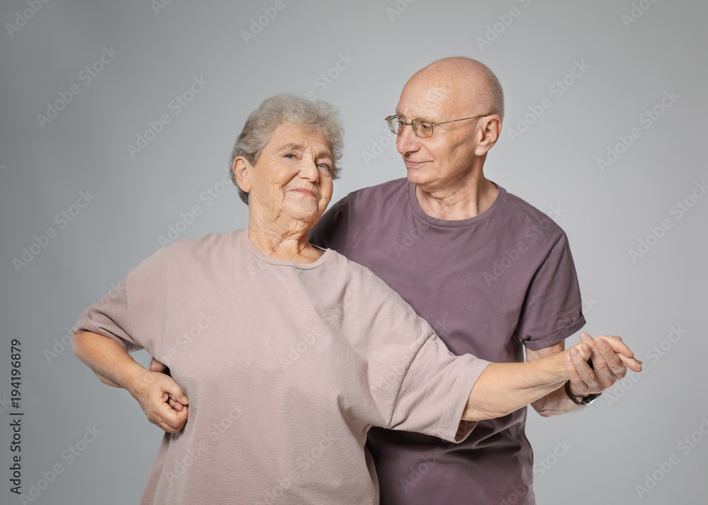 Cute elderly couple dancing against grey background Cute elderly couple dancing against grey background