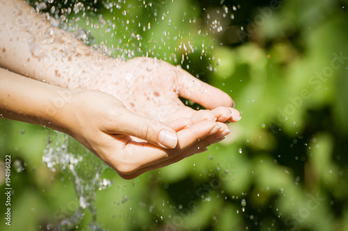 Woman washing hand outdoors. Natural drinking water in the palm. Young hands with water splash, selective focus