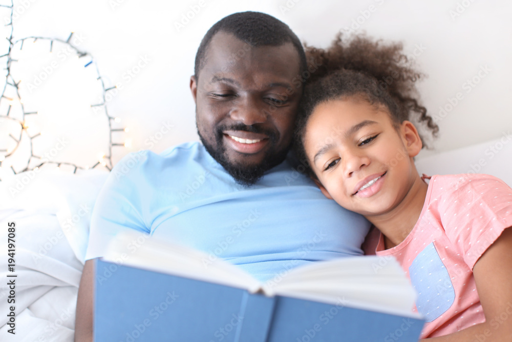 African American man reading bedtime story to his daughter in bed African American man reading bedtime story to his daughter in bed