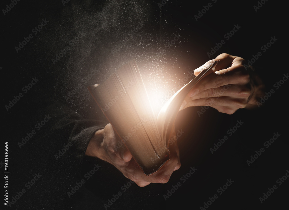 Priest with old Bible on black background, closeup - obrazy, fototapety, plakaty 