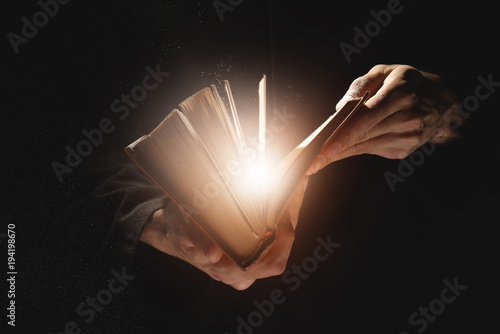 Priest with old Bible on black background, closeup