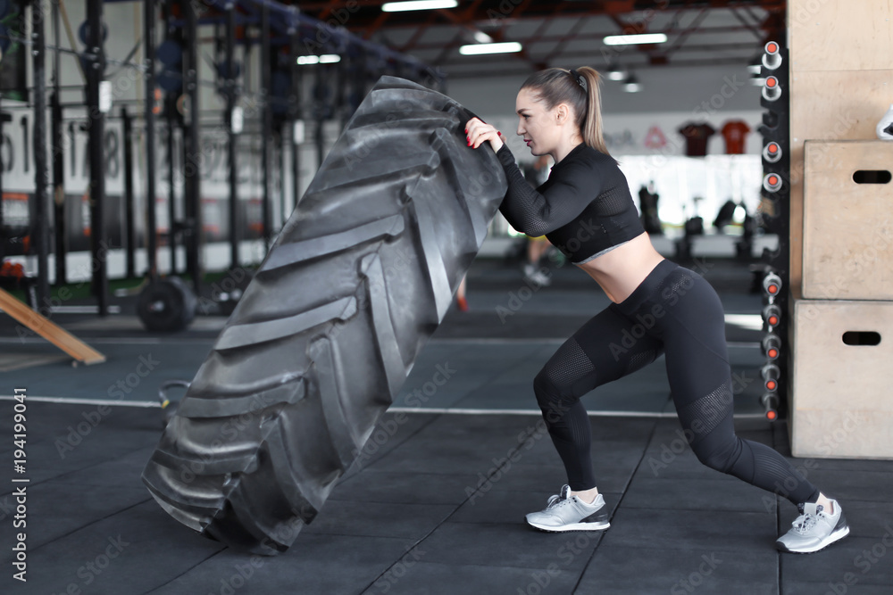 Obraz premium Young muscular woman flipping heavy tire in gym