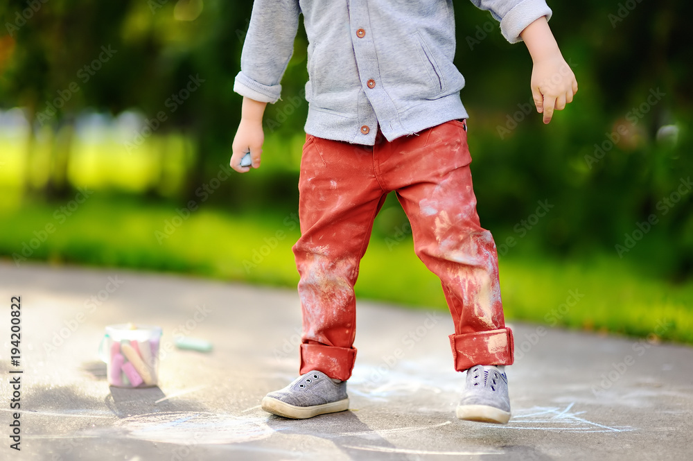 Obraz premium Close-up photo of little kid boy drawing with colored chalk on asphalt.