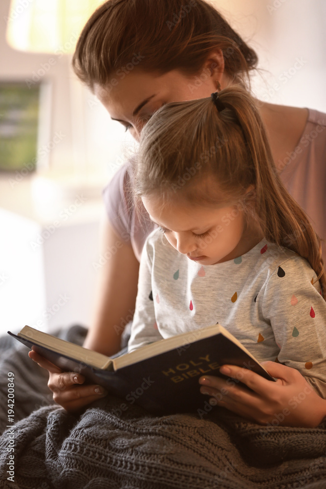 Religious Christian girl reading Bible with mother indoors Religious Christian girl reading Bible with mother indoors