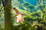 Woman climbing a tree in a forest dancing with Table Mountain in the background.