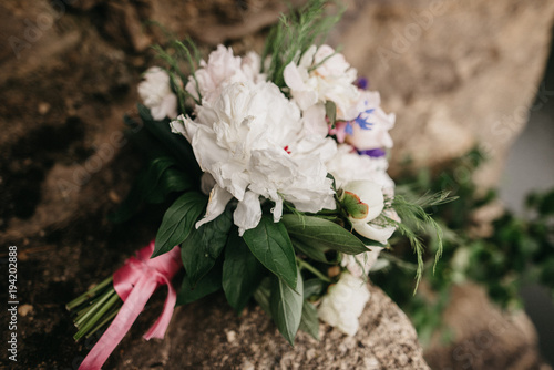 Wedding bouquet. Beautiful wedding bouquet of white peonies and greenery with pink ribbon lies on a large rock. Top view