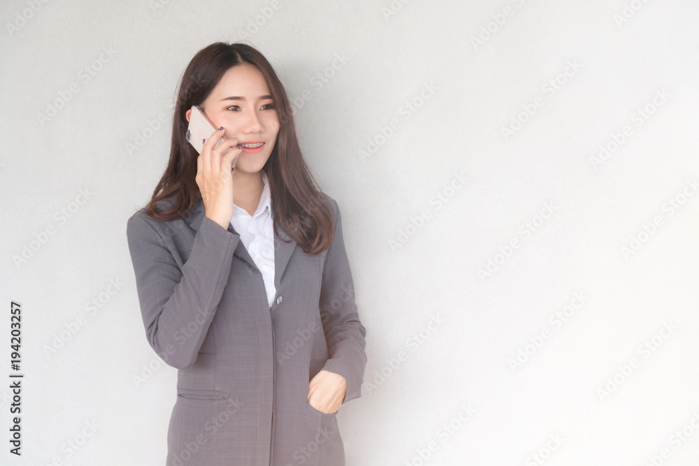 Portrait of a Attractive young Asian businesswoman wearing a suit and talking on mobile phone with copy space on a gray background. Portrait of a Attractive young Asian businesswoman wearing a suit and talking on mobile phone with copy space on a gray background.