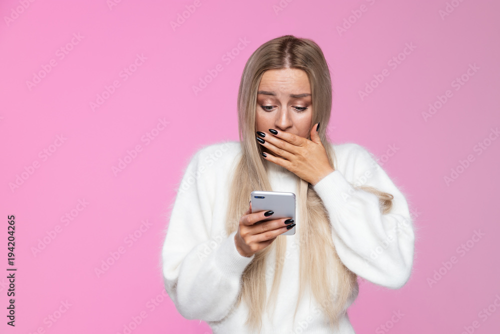 Anxious woman covers mouth in shock, holding and looking at mobile smart phone, surprise reaction on her face. Awkwardness gestures, expression concept. Isolated Anxious woman covers mouth in shock, holding and looking at mobile smart phone, surprise reaction on her face. Awkwardness gestures, expression concept. Isolated
