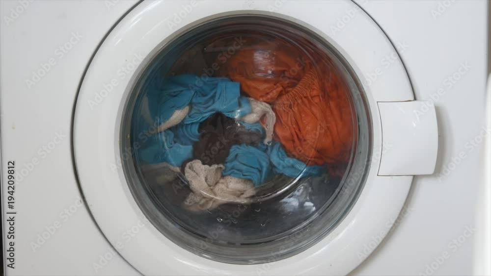 Washing machine door with rotating garments inside. focus in the center of dirty laundry and washing machine on the frame Washing machine door with rotating garments inside. focus in the center of dirty laundry and washing machine on the frame
