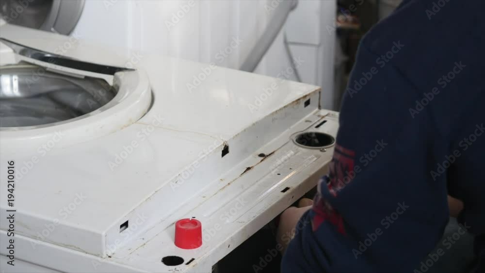 A repairman is completely dismantling a control panel on the washing machine. He needs to fix the whole device. A repairman is completely dismantling a control panel on the washing machine. He needs to fix the whole device.