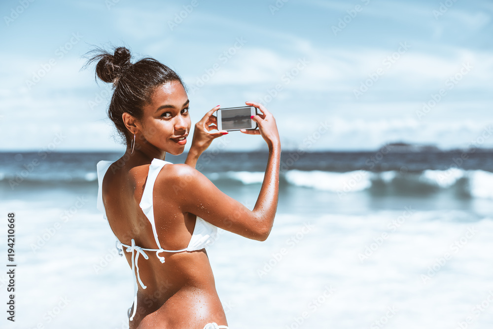 Rear view of svelte young Brazilian girl in swimsuit with wet skin,  half-turned and looking