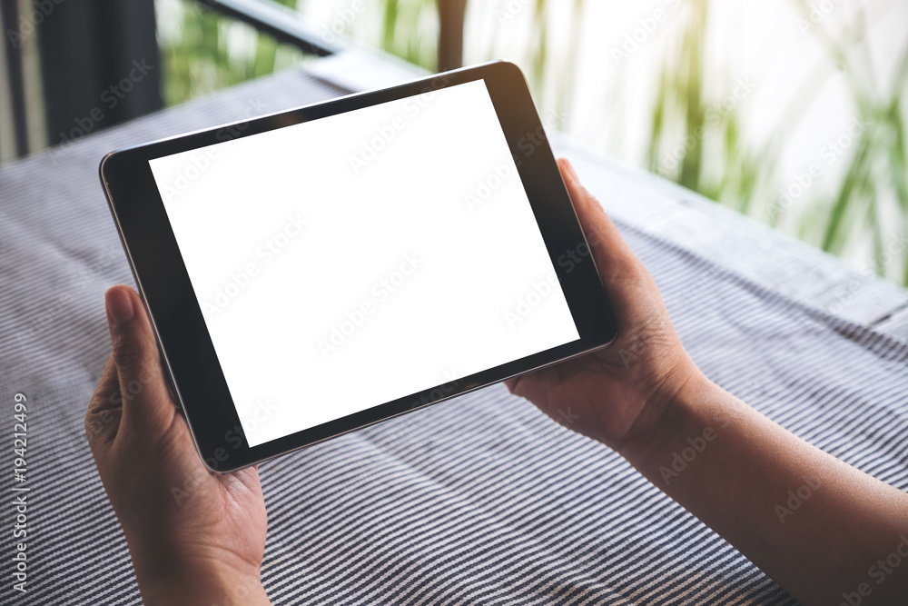 Mockup image of hands holding black tablet pc with blank white desktop screen on table with blur background in cafe Mockup image of hands holding black tablet pc with blank white desktop screen on table with blur background in cafe