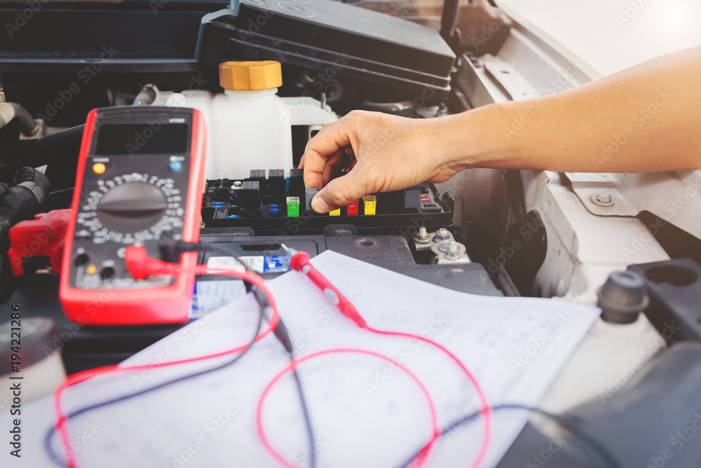 Auto mechanic using digital multimeter to check the fuse in a car,check voltage level car battery. Auto mechanic using digital multimeter to check the fuse in a car,check voltage level car battery.