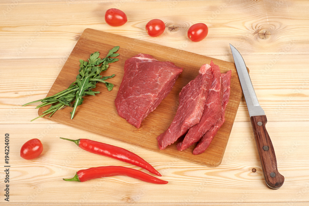 Sliced raw beef on cutting board and vegetables