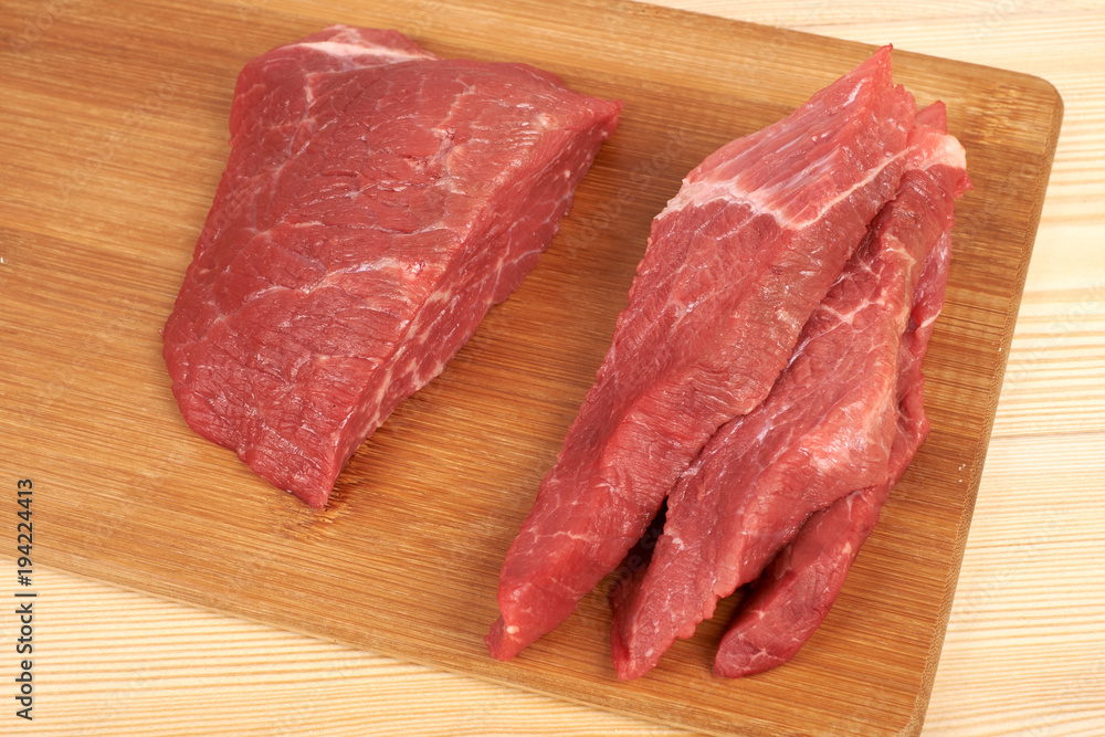 Raw beef piece and slices on wooden cutting board