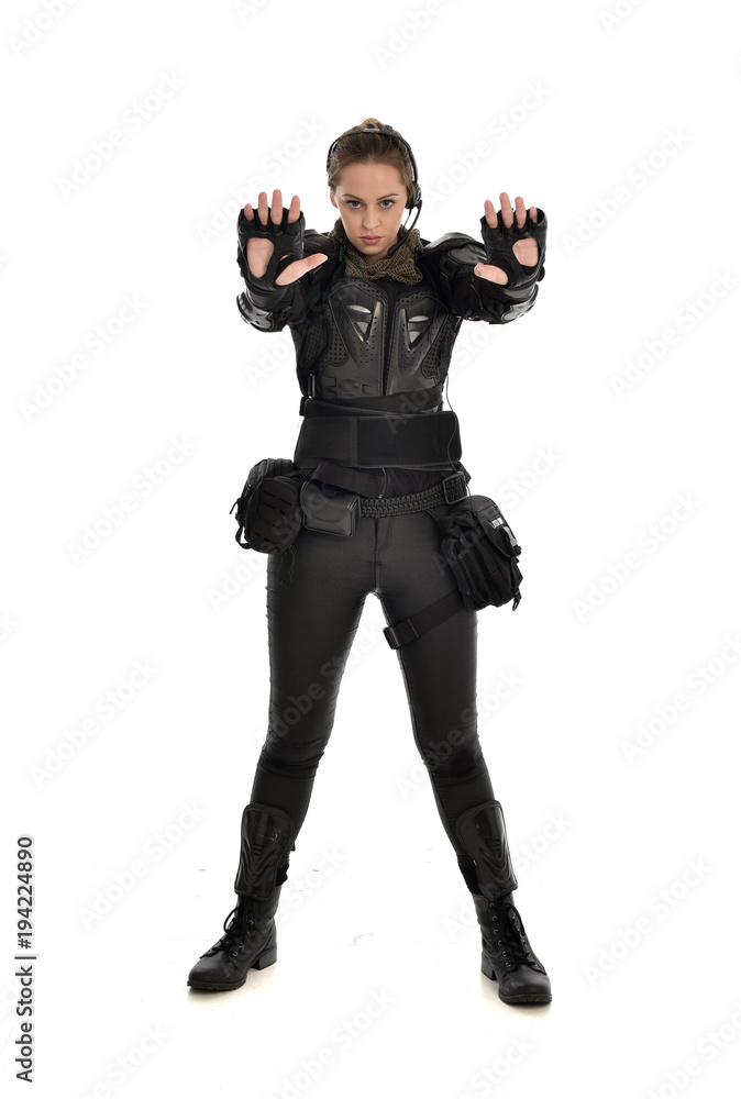 full length portrait of female soldier wearing black tactical armour with arms raised, isolated on white studio background. full length portrait of female soldier wearing black tactical armour with arms raised, isolated on white studio background.