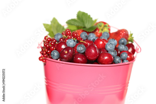 Berry season.bright pink bucket with berries of strawberries, blueberries, cherries, red currants isolated on white background. Harvest of berries. Delicious ripe berries in a pink bucket