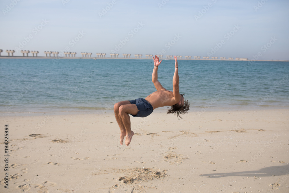 Young man doing somersault on the beach.